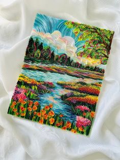 a painting of colorful flowers and trees on a white sheet with water in the background