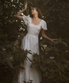 a woman in a white dress standing among trees