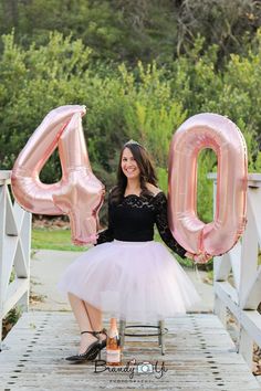 a woman in a tutu holding up the number 40 balloon while standing on a bridge