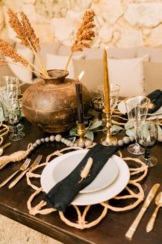 the table is set with black and white plates, silverware, gold candlesticks