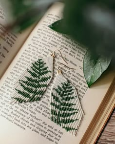 an open book with some green leaves on it and a pair of earrings hanging from the pages