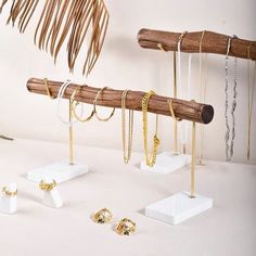 a collection of jewelry is displayed on white pedestals next to a palm tree branch