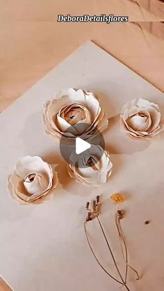 three paper flowers sitting on top of a piece of paper next to scissors and thread