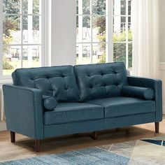 a blue couch sitting on top of a wooden floor in front of two large windows