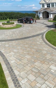 a driveway with two cars parked in front of it and the ocean in the background