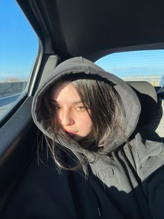 a woman wearing a hoodie in the back seat of a car looking at the camera