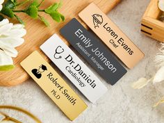 three personalized name tags sitting on top of a wooden cutting board next to flowers