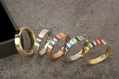 five different colored rings sitting next to each other on top of a gray surface with a black box in the background