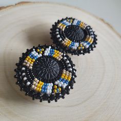 two black and yellow beaded earrings sitting on top of a piece of wood