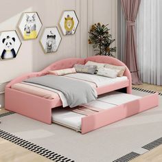 a pink bed sitting on top of a wooden floor next to a wall with pictures