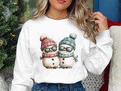 Cute Snowman Shirt, Funny Snowman Sweater, Christmas Snowman Hoodie, Christmas Snowman Sweatshirt, Christmas Gift for Anyone Embrace the winter season with our Cute Snowman T-Shirt. Featuring a delightful design of two snowmen in cozy hats and scarves, this tee is perfect for holiday celebrations or casual wear. The playful snowmen with sunglasses add a touch of fun and whimsy to your wardrobe. Ideal as a Christmas gift, this shirt will bring smiles and joy to anyone who wears it. Celebrate winter in style with this charming snowmen graphic tee. Product Features: Fabrication: 100% ring-spun cotton - Light fabric (4.5 oz/yd² (153 g/m Seams: Without side seams Fit: Eurofit Sizing: Runs true to size Label: Tear-away label Cozy Hats, Snowman Sweatshirt, Snowman Sweater, Funny Snowman, Snowman Shirt, Hats And Scarves, Cozy Hat, Sweatshirt Christmas, Cute Snowman