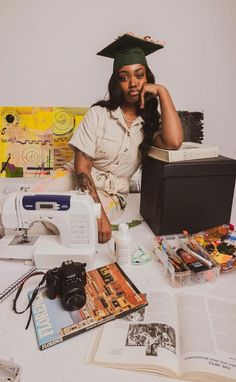 a woman in a graduation cap sitting at a sewing machine with books and other crafting supplies