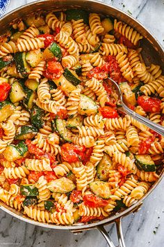 a pan filled with pasta and vegetables on top of a marble countertop next to a spoon