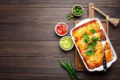 an enchilada dish on a cutting board with salsa and guacamole