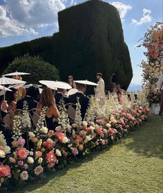 a group of people sitting under umbrellas on top of a lush green field next to flowers