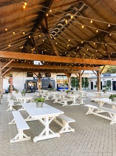 tables and benches are set up under a covered area with lights strung from the roof