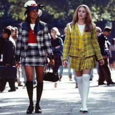 two women walking down the street in short skirts and plaid jackets, one wearing knee high socks