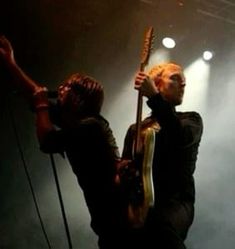 two people standing on stage with guitars in their hands