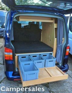 the back end of a blue van with its doors open and several storage bins in it