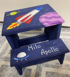 a blue wooden bench with an image of a rocket ship and space shuttle painted on it