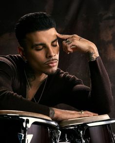 a man sitting in front of a drum set with his hand on the top of it