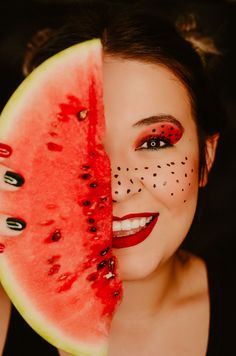 a woman is holding a slice of watermelon with black dots on her face