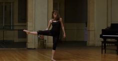 a young woman is practicing her moves on the floor in front of a grand piano