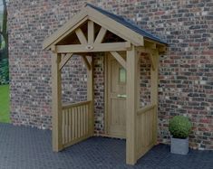 a small wooden gazebo next to a brick wall with a potted plant in it