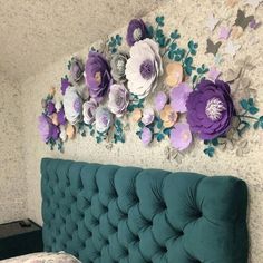 a green headboard with purple and white paper flowers on the wall above it, next to a bed