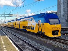 a blue and yellow train traveling down tracks next to a tall building with power lines above it