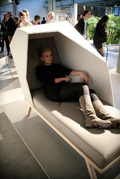 a woman is sitting on a couch in a room with people standing around and looking at the camera