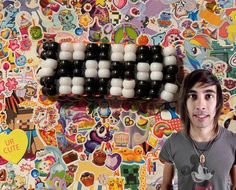 a young man standing in front of a wall covered with stickers and magnets