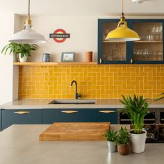 a kitchen with yellow and blue cabinets, potted plants on the counter top and hanging lights over the sink