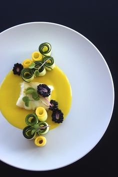 a white plate topped with food on top of a yellow sauce covered in green and yellow swirls