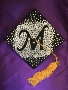 a black and white graduation cap with the letter m on it, decorated with beads