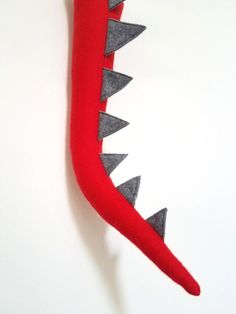 a red and gray stuffed animal with spikes on it's head, sitting against a white wall