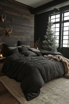 a bed with black comforter and pillows next to a christmas tree in a room