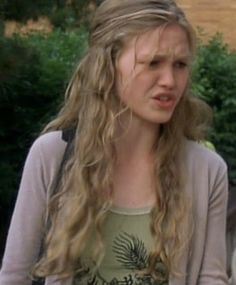 a woman with long blonde hair standing in front of bushes