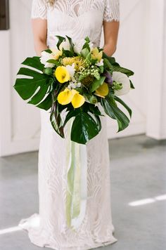 a woman in a white dress holding a bouquet of flowers and greenery on her wedding day