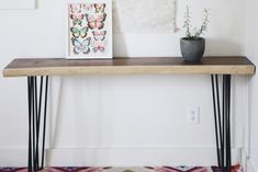 a wooden table with two plants on it and pictures hanging above the top, along with an upholstered bench