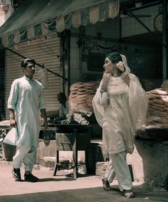 a man and woman walking down the street in front of an outdoor market with goods for sale