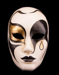 a white mask with black and gold designs on it's face, against a black background