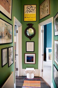 a hallway with green walls and pictures hanging on the wall, along with an area rug