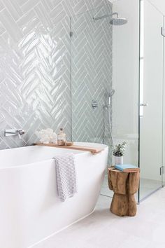 a white bath tub sitting next to a wooden stool in a bathroom under a shower