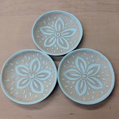 three blue plates sitting on top of a wooden table next to each other and one has a flower design on it