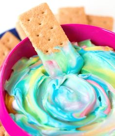 a pink bowl filled with blue and green dip next to crackers on the side