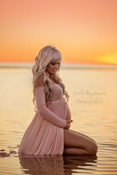 a pregnant woman sitting in the water at sunset