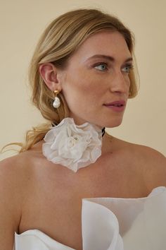 a woman wearing a white dress with a flower on the neck and earrings in front of her face