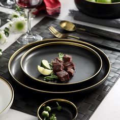 a black plate topped with meat and veggies on top of a white table