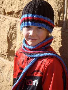 a young boy wearing a knitted hat and scarf standing in front of a stone wall